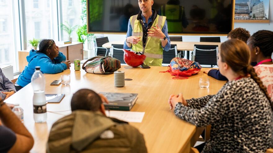 A man in a high vis vest is teaching a table of young people in a classroom 