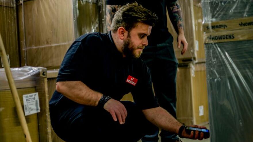 A man bending down in a warehouse unwrapping shrinkwrap with a knife