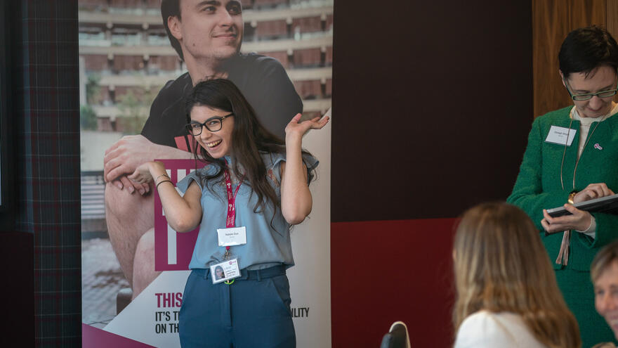 A picture of a woman standing in front of an audience, laughing. 