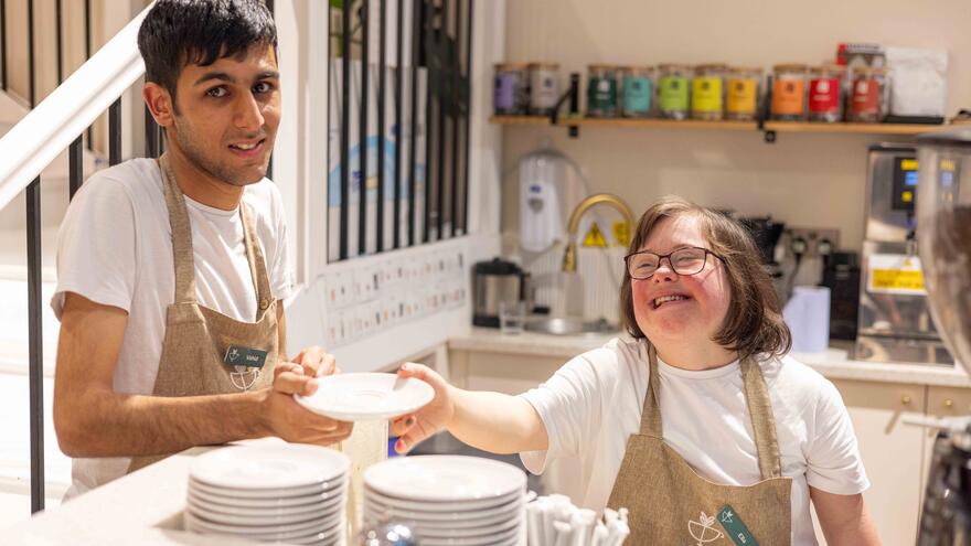 A young man and woman working in a kitchen, passing plates between each other.
