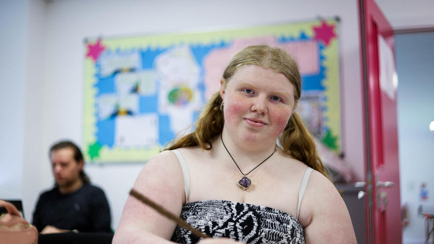 A Mencap Training Academy supported internship learner sat at a desk. She is smiling as she writes on some paper.