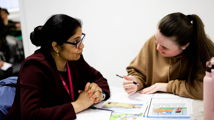 A tutor helping a supported internship learner with some work, while sitting at a desk.