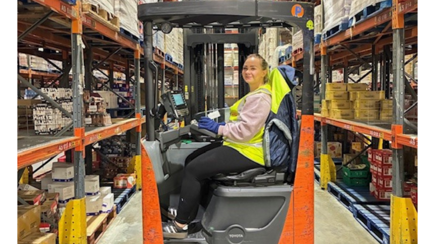 An image of a young woman operating a piece of machinery in a GXO warehouse where Mencap deliver a supported internship programme.